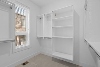 A white closet with shelves and a window with blinds.